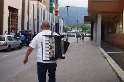 Čovjek hoda ulicom sa harmonikom na leđuma.