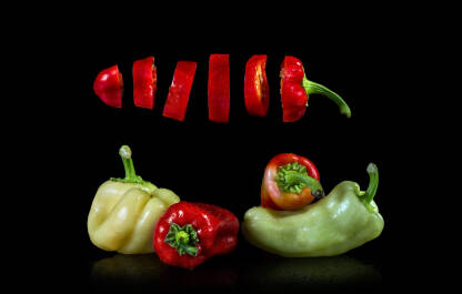 Crvene i žute paprike Narezana crvena paprika lebdi u zraku iznad dvije crvene i dvije žute paprike. Crvene i žute paprike poprskane vodom na crnoj podlozi.