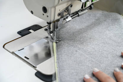 Žena šije tekstil šivaćom mašinom. Radnica u fabrici. Žena šije tekstil šivaćom mašinom. Radnica radi u fabrici. Krupni plan djevojčinih ruku dok šije tkaninu u fabrici.