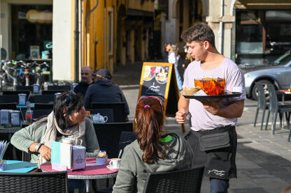 Konobar poslužuje goste kafića Konobar poslužuje goste kafića. Konobar nosi piće.