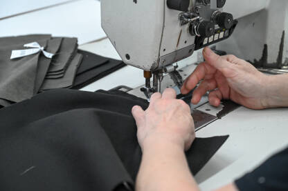 Žena šije tekstil šivaćom mašinom. Radnica radi u fabrici.