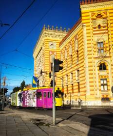 Vijećnica, Sarajevo Sarajevska Vijećnica obasjana jutarnjim suncem i tramvaj koji prolazi pored nje.