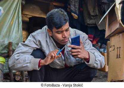 Migrant skraćuje bradu Migrant uređuje bradu makazama. Izbjeglica se ogleda na telefonu i makazama skraćuje bradu.
