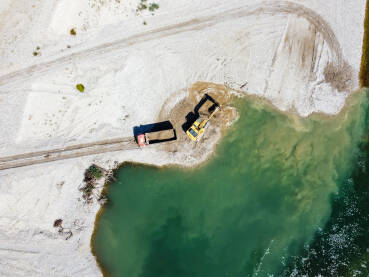DJI_0110 Bager kopa i utovaruje pijesak u kamion na obali rijeke. Teški strojevi rade u kamenolomu pijeska. Snimak dronom na bager i kamion koji utovaruju šljunak u prirodi. Zagađenje okoliša i vode