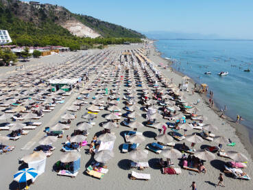 Mnogo ljudi na pješčanoj plaži i u moru. Suncobrani i ležaljke na obali uz more, snimak dronom. Jadransko more, Shengjin, Albanija. Turisti na plaži.