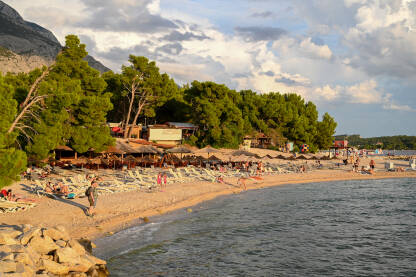 Makarska, Hrvatska. Ljudi uživaju na plaži uz more. Turisti Makarska, Hrvatska. Ljudi uživaju na plaži uz more. Turisti na pješčanoj plaži tokom zalaska sunca. Godišnji odmor.
