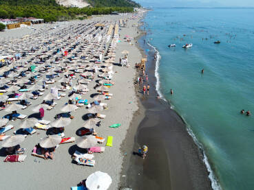Mnogo ljudi na pješčanoj plaži i u moru. Suncobrani i ležaljke na obali uz more, snimak dronom. Jadransko more, Shengjin, Albanija. Turisti na plaži.