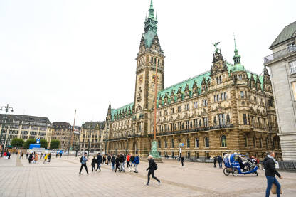 Hamburg, Njemačka: Ljudi šetaju centrom grada. Vijećnica. Hamburg, Njemačka: Ljudi šetaju centrom grada. Grupa ljudi i turista u šetnji glavnim trgom u Hamburgu. Zgrada gradske vijećnice.