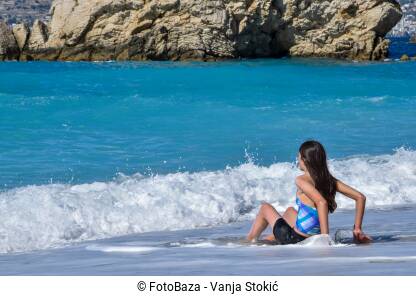 Djevojka na plaži Djevojka sjedi sama na plaži u Ksamilu, Albanija. Uživanje u morskim talasima. Djevojčica sjedi na obali mora.