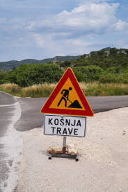 Znak za košnu trave na putu na praznoj cesti.