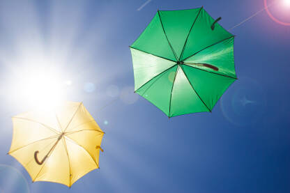 Žuti i zeleni kišobran, zakačeni na žicu iznad ulice. Umjetnička instalacija. Intervencija u prostoru.