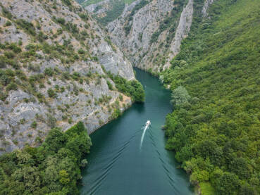 Duboki kanjon rijeke između planina, snimak dronom. Kanjon Matka, Sjeverna Makedonija. Turistički brodić plovi rijekom.