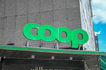 Logo supermarketa Coop ispred maloprodajnog objekta. Ulaz u Coop prodavnicu sa osvijetljenim logotipom. Coop je glavni maloprodajni brend koji posluje širom Skandinavije - Švedske, Danske, Norveške.
