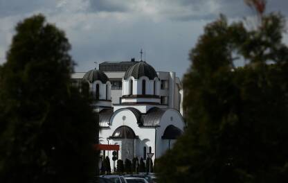 Crkva u daljini izmedju dva zelena drveta Crkva vidljiva izmedju drveca, plavo nebo, pejzaz