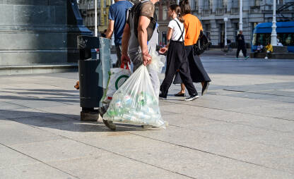 Muškarac sakuplja plastičnu ambalažu i boce u gradu. Reciklaža plastike i smeća.