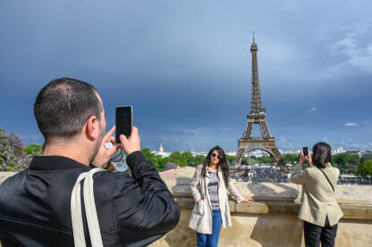 Turisti ispred Ajfelovog tornja Pariz, Francuska: Turisti se fotografišu ispred Ajfelovog tornja. Popularna turistička destinacija.