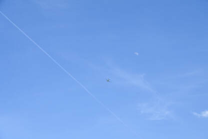 AK1_7165 (2) Avion na plavom nebu među oblacima i tragovima aviona. Putovanje. Komercijalni mlazni avion koji leti na nebu s mjesecom u daljini.