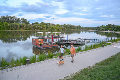 Szentendre, Mađarska: Ljudi šetaju uz Dunav. Szentendre, Mađarska: Brod na Dunavu u Szentendreiju. Ljudi šetaju uz rijeku.