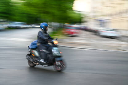 Čovjek se brzo kreće na skuteru Čovjek se brzo kreće na motociklu na ulici. Vožnja skuterom po gradu. Vozač motocikla. Blurana fotografija.
