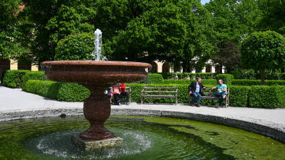 Fontana Fontana sa vodom u parku. Ljudi sjede na klupama u parku blizu fontane. Osvježenje tokom toplih ljetnih dana.