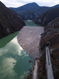 Razni oblici komunalnog otpada nagomilani u rijeci Drini, vidljivi na površini i uz obalu.