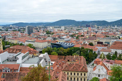 Graz, Austrija: Panoramski pogled na grad. Zgrade, kuće, ulice i crveni krovovi Graza. Zgrada Kunsthausa ili muzeja umjetnosti.
