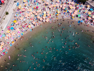 Mnogo turista u moru i na plaži na vrhuncu ljetne turističke sezone. Gomila ljudi koji se kupaju u moru. Ljudi u kupaćim kostimima na plaži, snimak dronom. Neum, BiH.