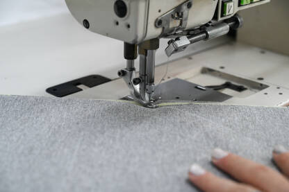 Žena šije tekstil šivaćom mašinom. Radnica u fabrici. Žena šije tekstil šivaćom mašinom. Radnica radi u fabrici. Krupni plan djevojčinih ruku dok šije tkaninu u fabrici.