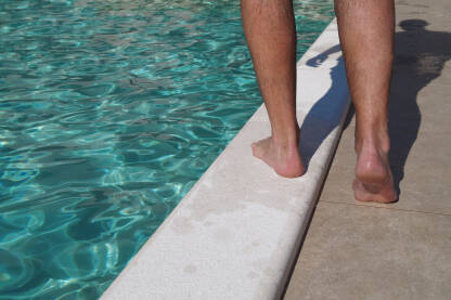 Noge čovjeka koji hoda uz rub bazena.