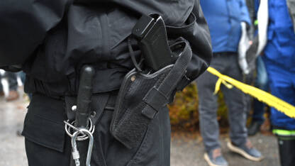 Pištolj na pojasu policajca na protestu. Pištolj u futroli pripadnika specijalnih policijskih snaga. Pištolj i palica policajca.