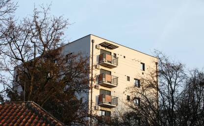 Bela stambena zgrada Zgrada slikana sa puta, sa strane je drvece, plavo nebo