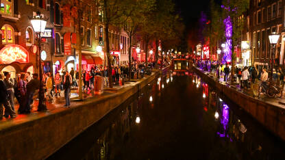 Amsterdam, Nizozemska Amsterdam, Nizozemska. Red light district noću. Zgrade, riječni kanal i turisti u gradu.