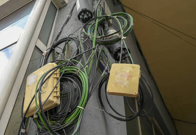 Žice od telefona, interneta, kablovske televizije i drugih servisa umotani u veliko klupko na fasadi zgrade. Kablovi na ulazu u zgradu.