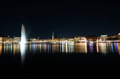 Hamburg, Njemačka. Zgrade u centru grada noću. Hamburg, Njemačka. Toranj gradske vijećnice, zgrade i Alster jezera noću. Cityscape. Refleksija svjetla u vodi.
