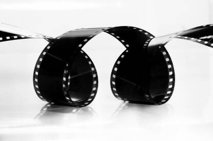 Kinematografska zakrivljena analogna filmska traka  na bijeloj pozadini. Historija filma i fotografije, vizualno pripovijedanje i nostalgija.