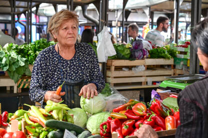 Starija žena prodaje voće i povrće na pijaci. Starija žena prodaje voće i povrće na pijaci. Svježe organsko povrće na tržnici.