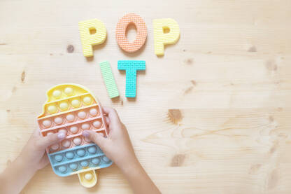 Pop it igračka Dječije ruke drže igračku pop it na stolu.