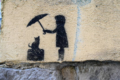 Djevojčica koja drži kišobran iznad mačke. Grafit.1 Simbol djevojčice koja drži kišobran iznad mačke. Grafit na zidu. Zaštita životinja.
