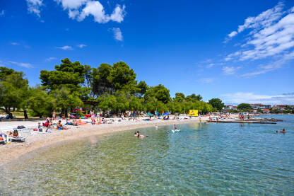 Turisti na moru. Ljudi se sunčaju na plaži. Vodice, Hrvatska: Turisti na moru. Ljudi plivaju u moru. Prepuna plaža. Turisti se sunčaju na plaži. Ljetni odmor. Grupa turista na plaži tokom toplog dana ljeti.