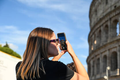 Djevojka mobilnim telefonom fotografiše Coloseum u Rimu. Turisti u gradu.