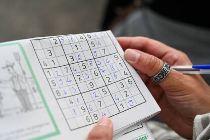 Mlada žena rješava sudoku zagonetku. Krupni plan žene koja drži olovku i rješava sudoku zagonetku. Osoba koja igra sudoku zagonetku. Djevojka igra sudoku.
