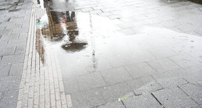 Refleksija osobe sa kišobranom u lokvi vode. Refleksija osobe sa kišobranom u lokvi vode. Kiša na asfaltnom putu. Kapljice kiše u lokvi. Ljudi sa hodaju sa kišobranom.