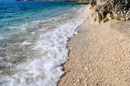 Pješčana plaža ljeti. More. Morski valovi se razbijaju o obalu. Pješčana plaža ljeti. Pjenasto mekani talasi.