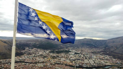 Državna zastava Bosne i Hercegovine. Zastava BiH. Državna zastava Bosne i Hercegovine se vijori na vjetru. Nacionalna zastava Bosne i Hercegovine na jarbol iznad grada Mostara, snimak dronom.