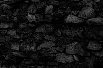 Teksturirana površina tamnog, gotovo crnog kamenog zida prikazana u krupnom planu.
