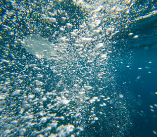 Perspektiva iz podvodnog svijeta, brojni mjehurići zraka koji se uzdižu kroz plavu vodu. Svjetlost se reflektira od mjehurića u moru. Podvodna kamera.