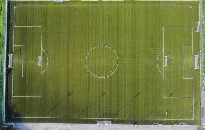 Fudbalsko igralište, snimak dronom. Stadion. Fudbalsko igralište. Zelena trava na stadionu, pogled odozgo. Fudbalski stadion sa bijelim linijama i golovima, snimak dronom.