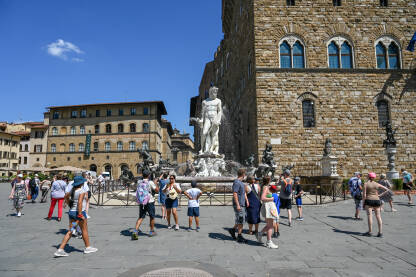 Firenca, Italija: Turisti na trgu. Neptunova fontana. Firenze, Italija: Turisti istražuju grad. Neptunova fontana na Piazza della Signoria. Ljudi šetaju trgom. Zgrade u centru grada.