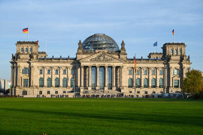 AK1_1202 Berlin, zgrada njemačkog parlamenta. Njemačke nacionalne zastave se vijore na jarbolu ispred zgrade Reichstaga u Berlinu, Njemačka. Njemački Bundestag.