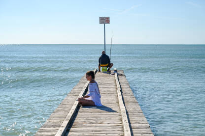 Djevojka meditira uz more dok ribolovac lovi ribu. Jadransko more u Italiji.